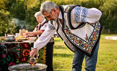 A man in folkloric costume cooks traditional food in Neamt County, Romania.