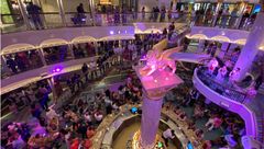 The cruise director speaks to guests in the Carnival Venezia's atrium to recognize the ship's officers.